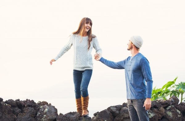 Happy Young Couple Having Fun Outdoors. Man helping attractive girlfriend over rock wall. Chivalry Concept, Romantic Date.