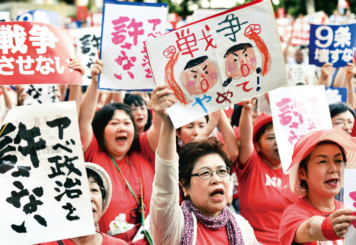 Civic group members hold placards and chant anti-government slogans in Tokyo on July 14, 2015 to protest against Prime Minister Shinzo Abe's controversial security bills. Abe, a robust nationalist, has pushed for what he calls a normalisation of Japan's military posture and wants to loosen restrictions that have bound the so-called Self-Defense Forces to a narrowly defensive role for decades.   AFP PHOTO / Yoshikazu TSUNO