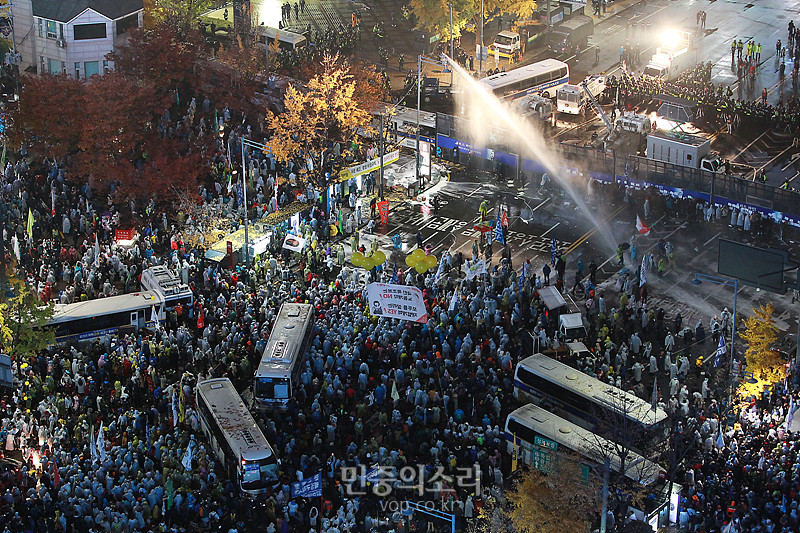 민중총궐기가 열린 14일 저녁 서울 중구 광화문 사거리 앞에서 광화문 광장으로 행진하는 시민들을 향해 경찰이 최루액이 섞인 물대포를 쏘고 있다. 시민들 사이로 밧줄을 이용해 끌어낸 경찰 버스가 6대가 보이고 있다.